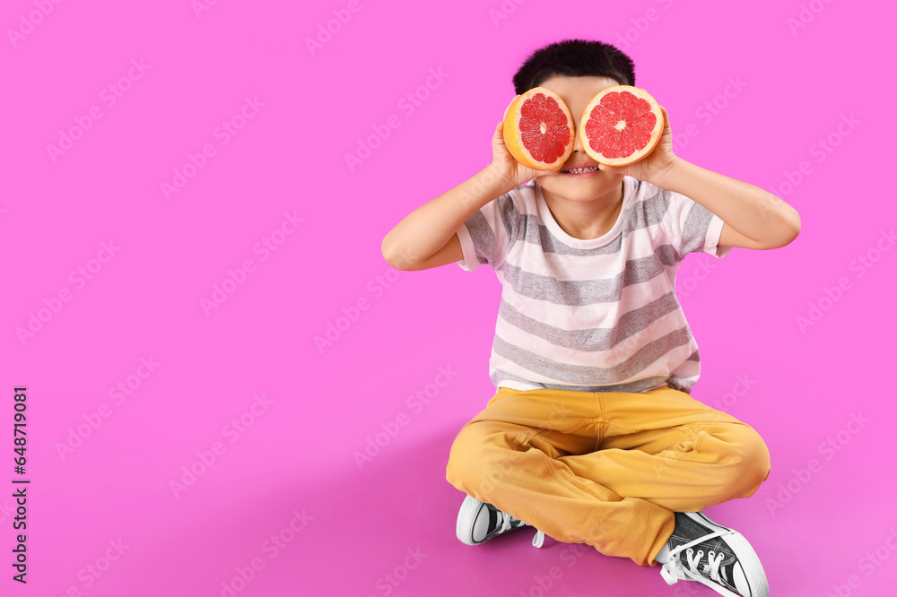 Little Asian boy with slices of fresh grapefruit sitting on purple background