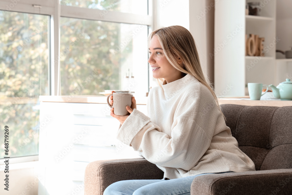 Young woman with cup of hot tea sitting in kitchen