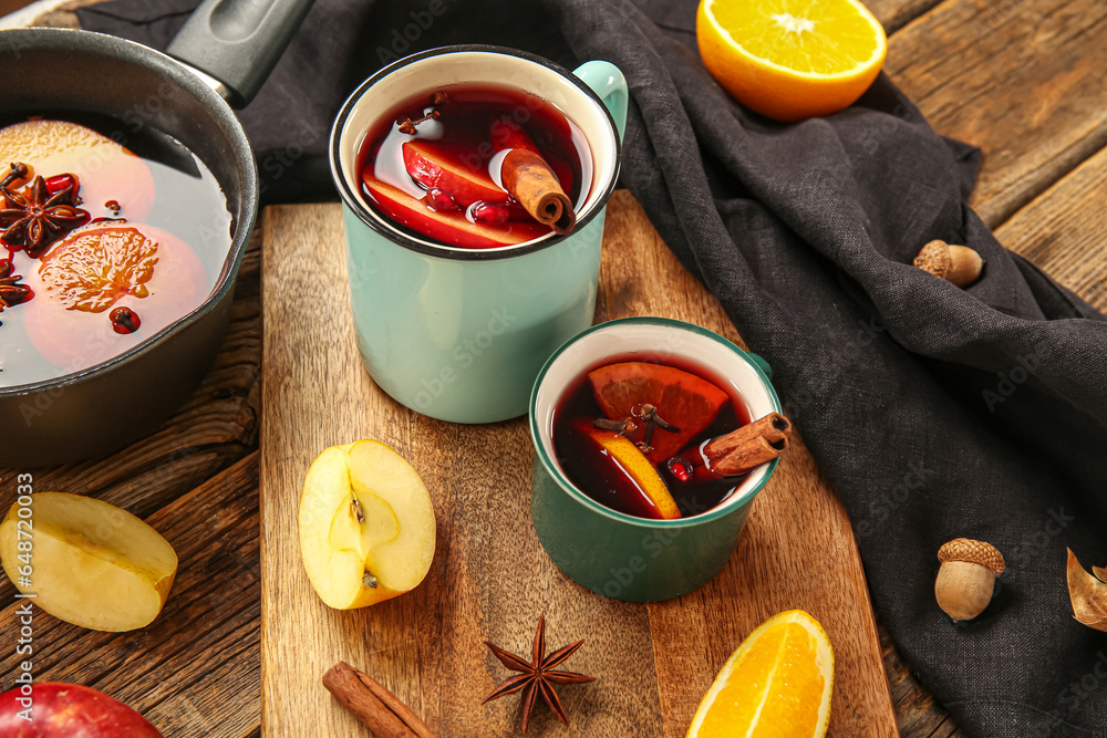 Cups of hot mulled wine with apple and orange on wooden background