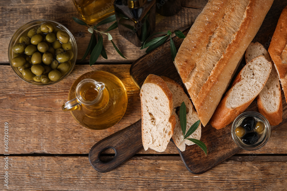 Board with bread, olives and oil on wooden background