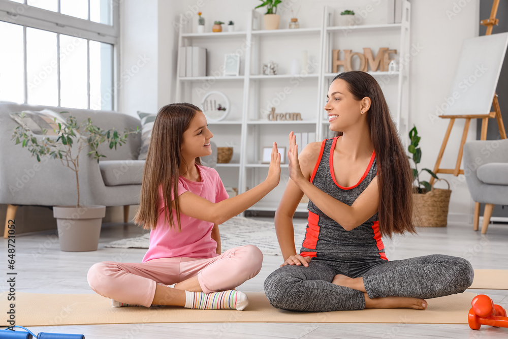 Sporty mother with her little daughter giving each other high-five at home