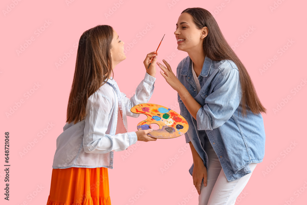 Little girl with paint palette and her mother on pink background