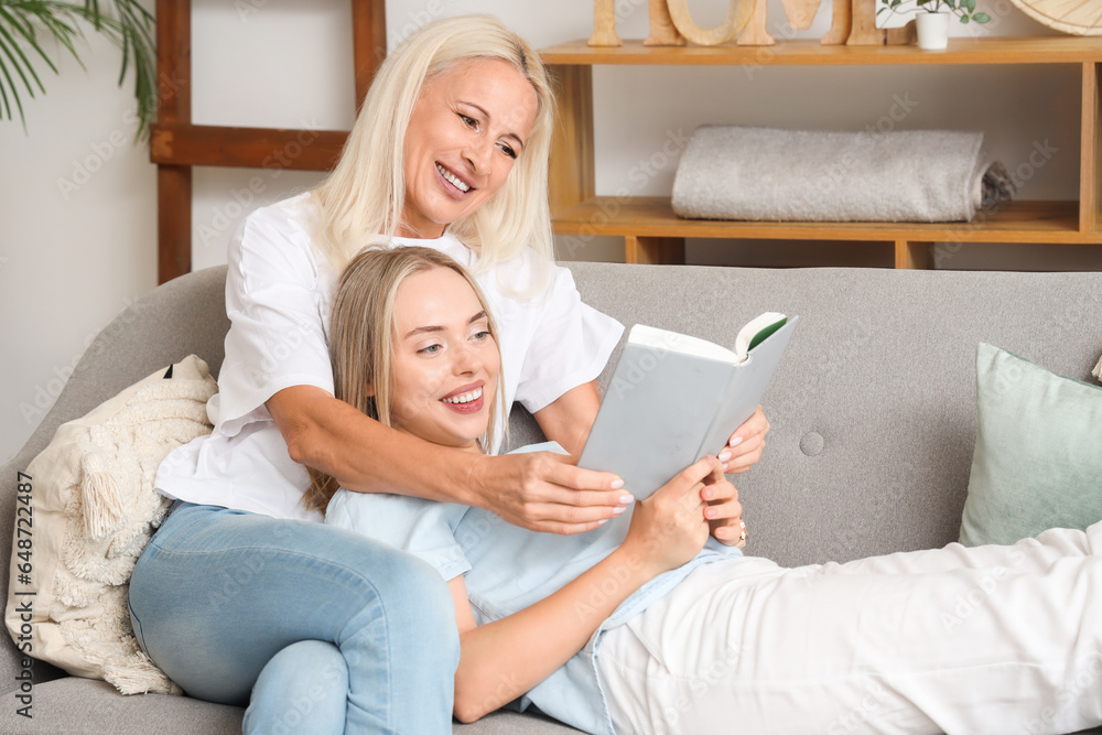 Young beautiful woman with her mother reading book together in living room