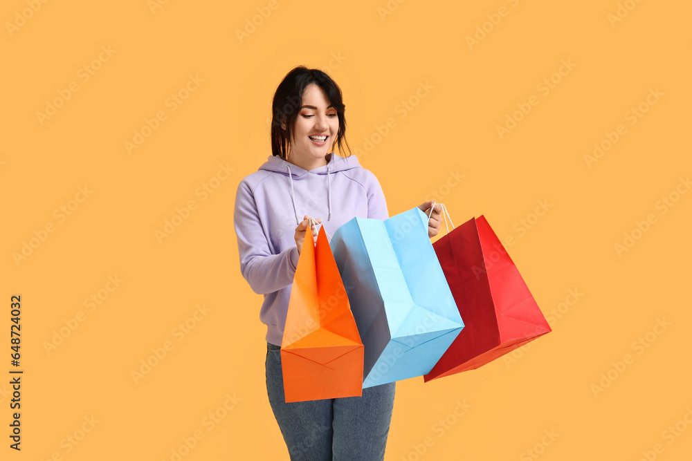 Beautiful happy woman with shopping bags on yellow background