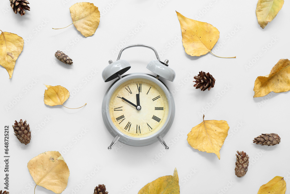 Alarm clock with autumn leaves on white background