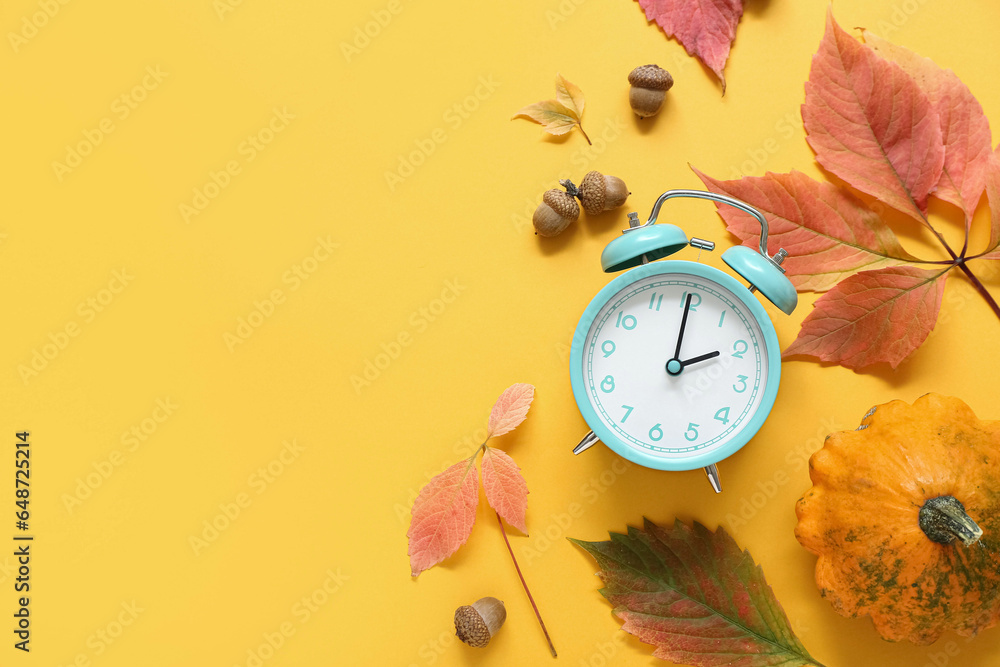 Alarm clock with autumn leaves and pumpkin on orange background