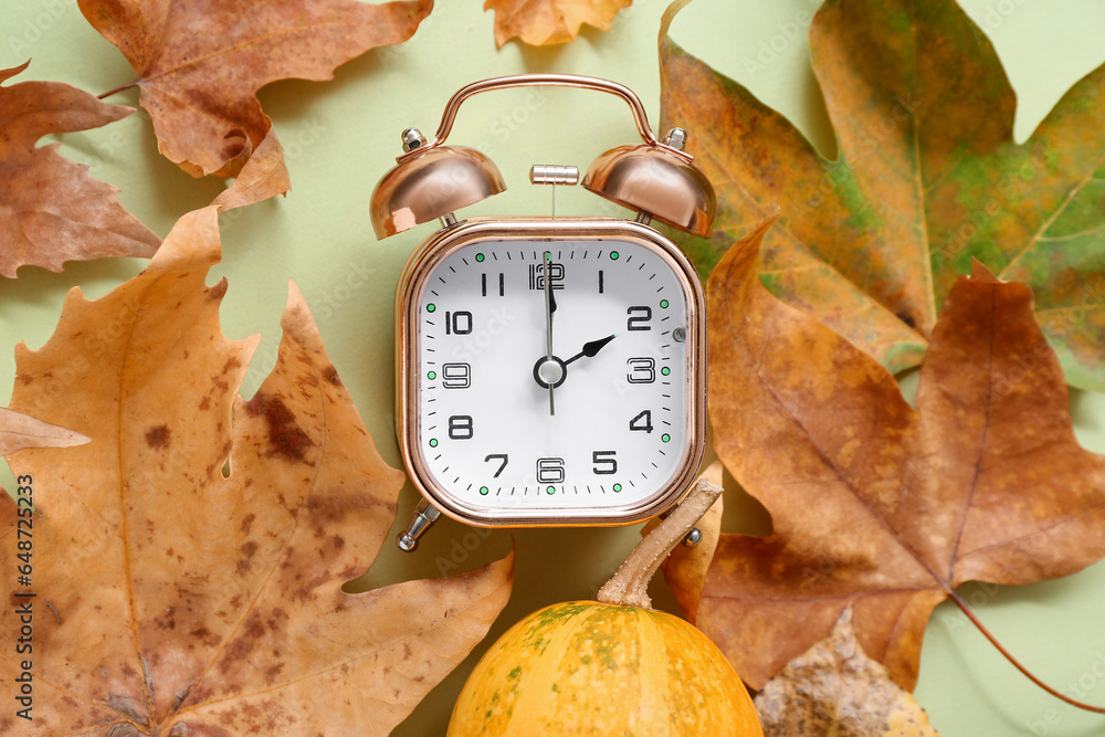 Alarm clock with autumn leaves and pumpkin on green background