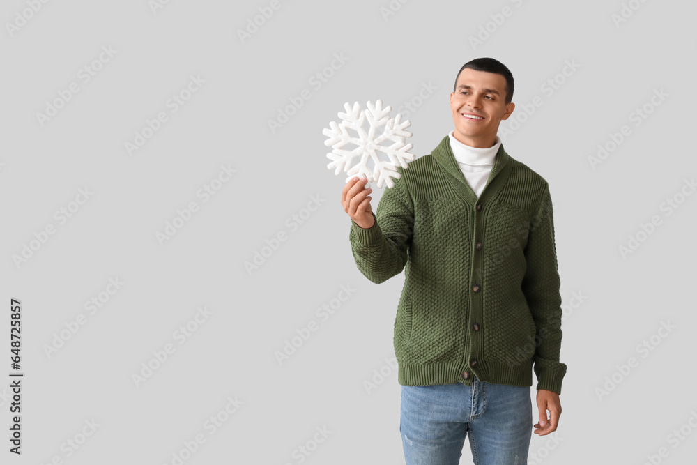 Young man in knitted sweater with snowflake on light background