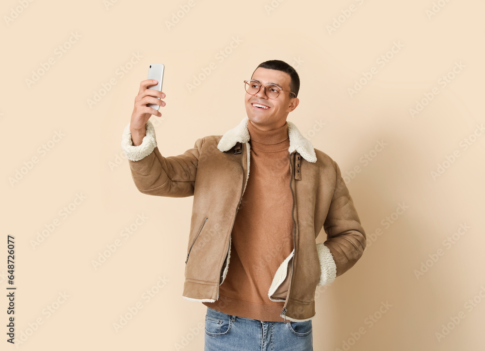 Young man in sheepskin jacket with mobile phone on beige background