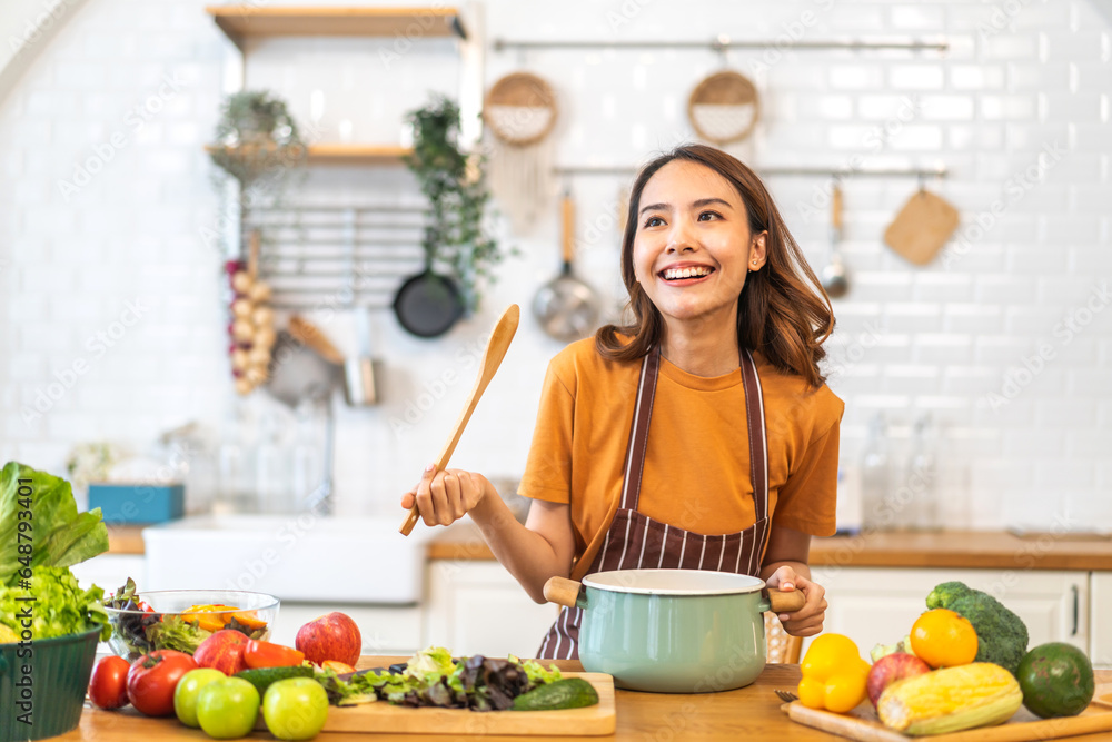 Young woman standing near stove and cooking, housewife, meal, chef, food.Happy woman looking and smelling tasting fresh delicious from soup in a pot with steam at white interior kitchen