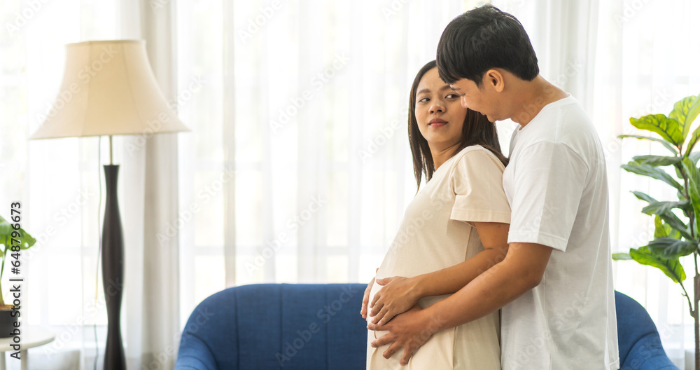 Romantic sweet asian couple husband hugging and smiling beauty asian pregnant wife.Man expecting with woman pregnancy hold to baby in belly at home