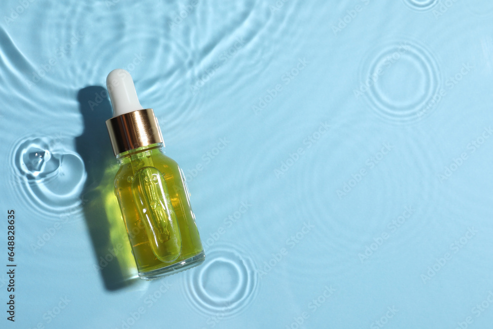 Bottle of cosmetic oil in water on light blue background, top view. Space for text