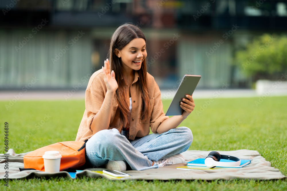 Cheerful young woman student chilling at park, using digital tablet