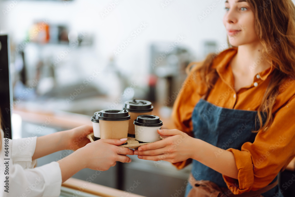 Close-up of a female baristas hands giving out a to-go drink order. The coffee shop owner gives orders to go. Takeaway drinks concept, small business.