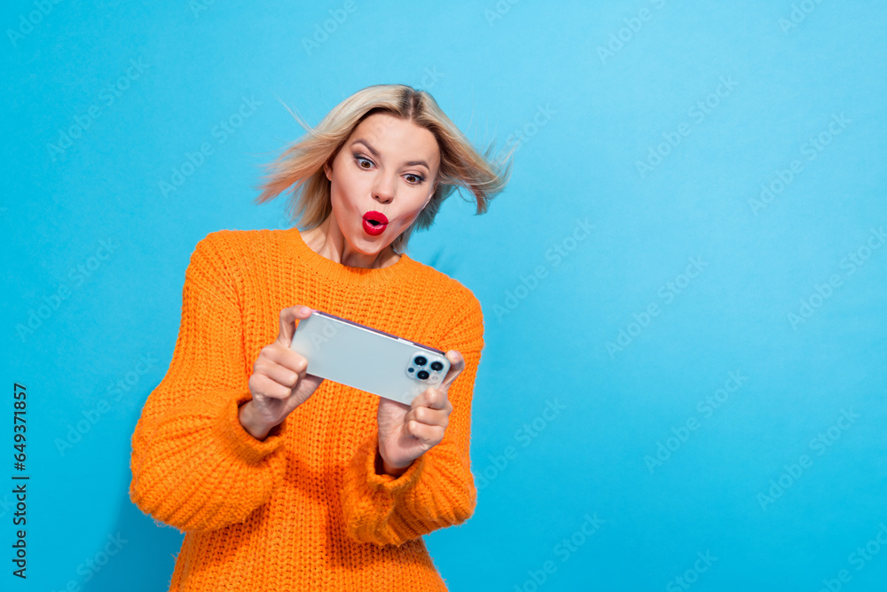 Portrait of overjoyed woman fluttering hair dressed knitwear sweater look at smartphone in hands isolated on blue color background