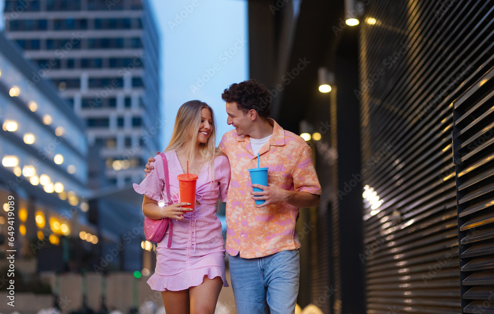 Gen Z couple in pink outfits leaving the cinema with drinks in hand.