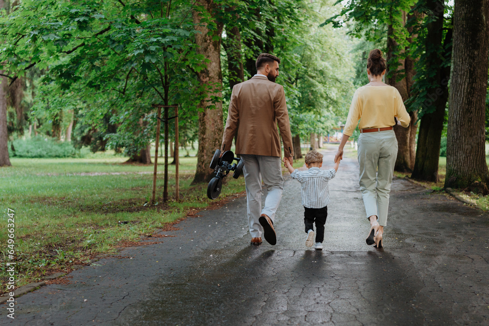 Young family with little son on walk in city park after work.