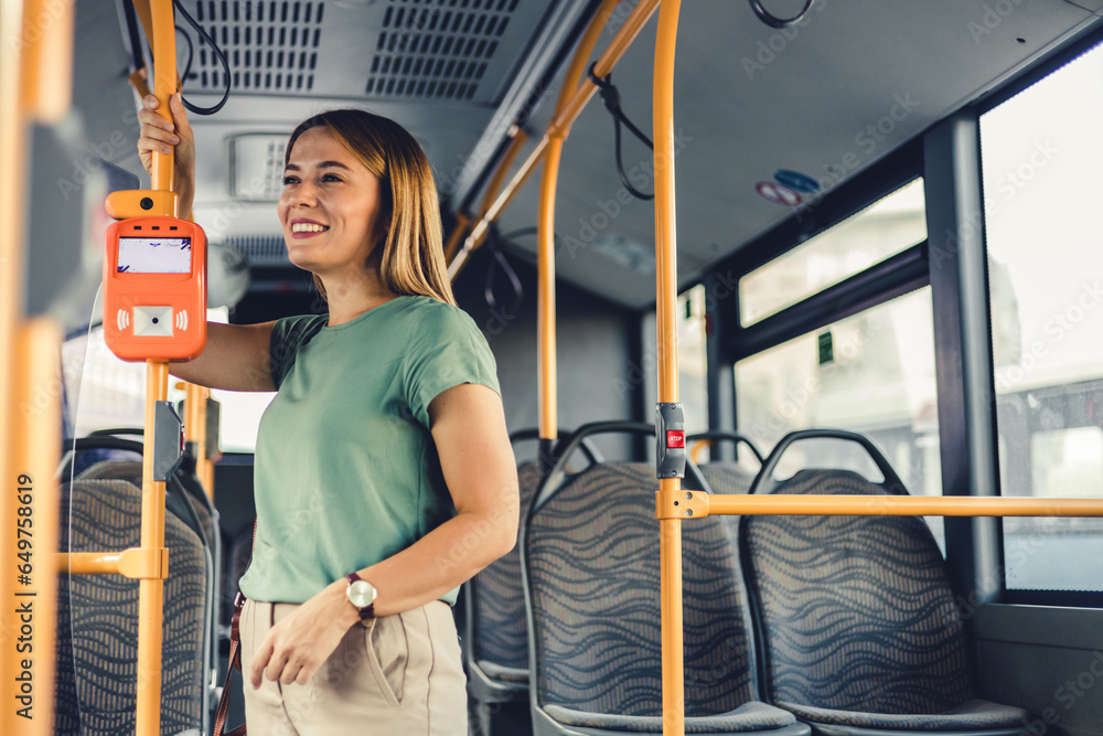 Female commuter holding handle and waves while standing in public transport. Beautiful woman enjoying trip at the public transport in the modern tram