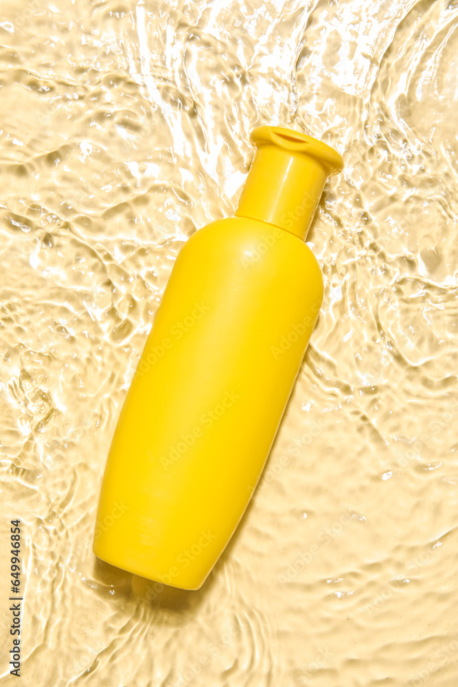 Bottle of sunscreen cream in water on color background