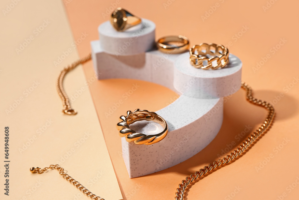 Decorative podiums with golden rings and necklace on color background