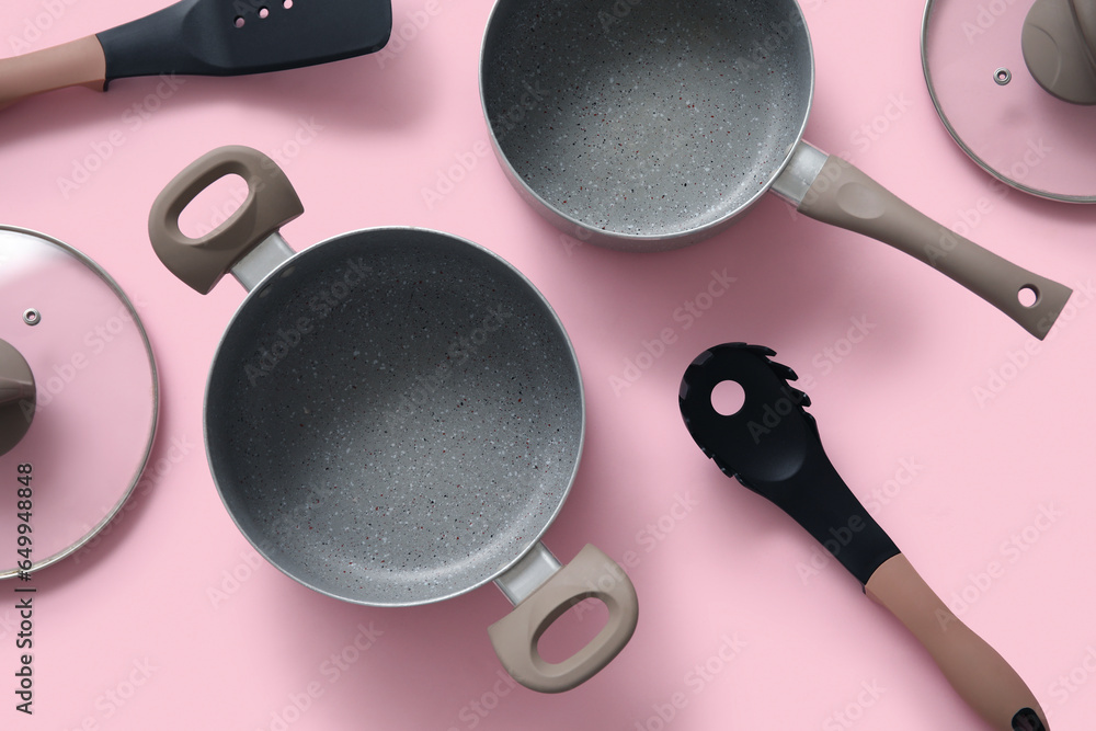 Cooking pots and kitchen utensils on pink background