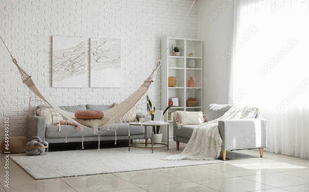 Interior of light living room with hammock and grey sofas