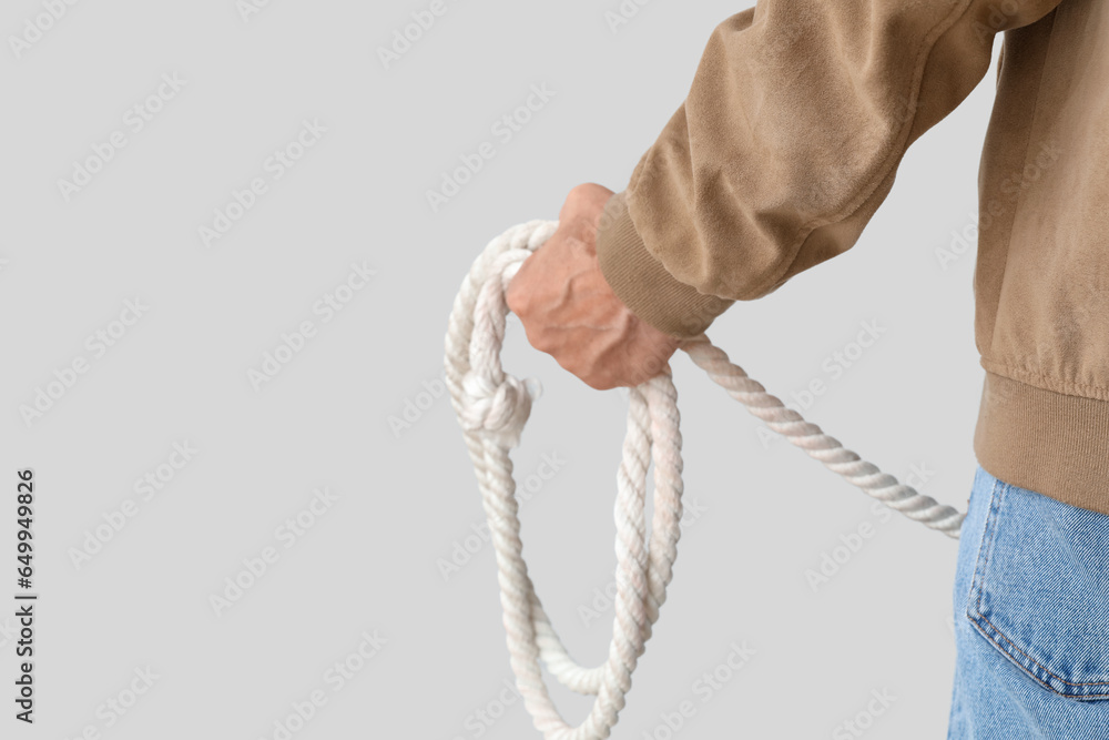 Mature cowboy with lasso on light background, closeup