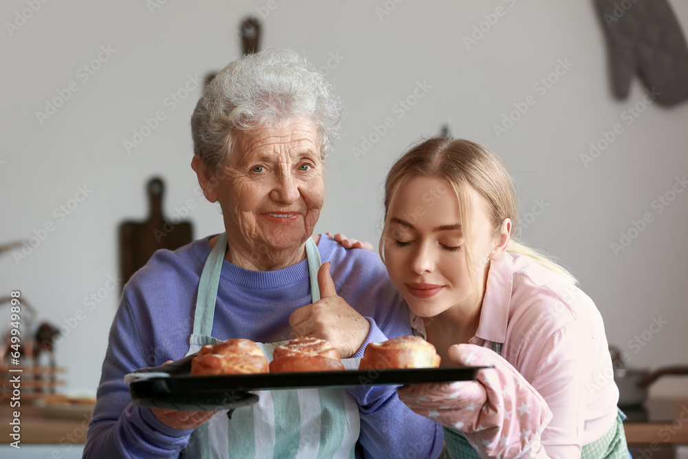 Young woman and her grandmother with baked buns in kitchen