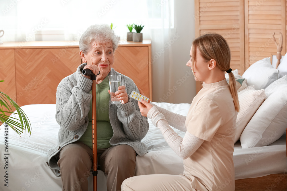 Young caregiver giving pills to senior woman in bedroom