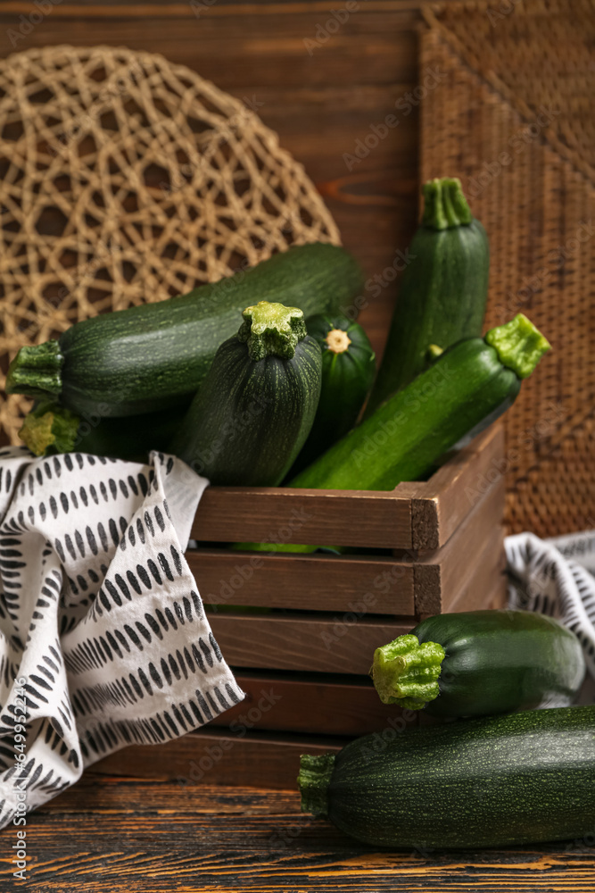 Box with many fresh zucchini on brown wooden background