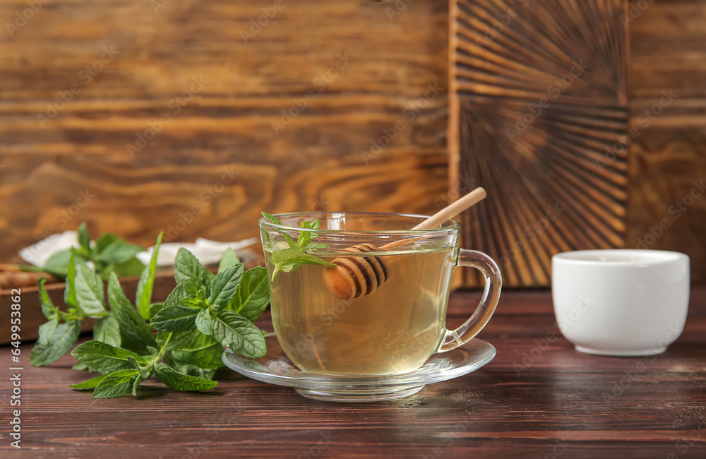 Cup of fresh mint tea with honey dipper on brown wooden table