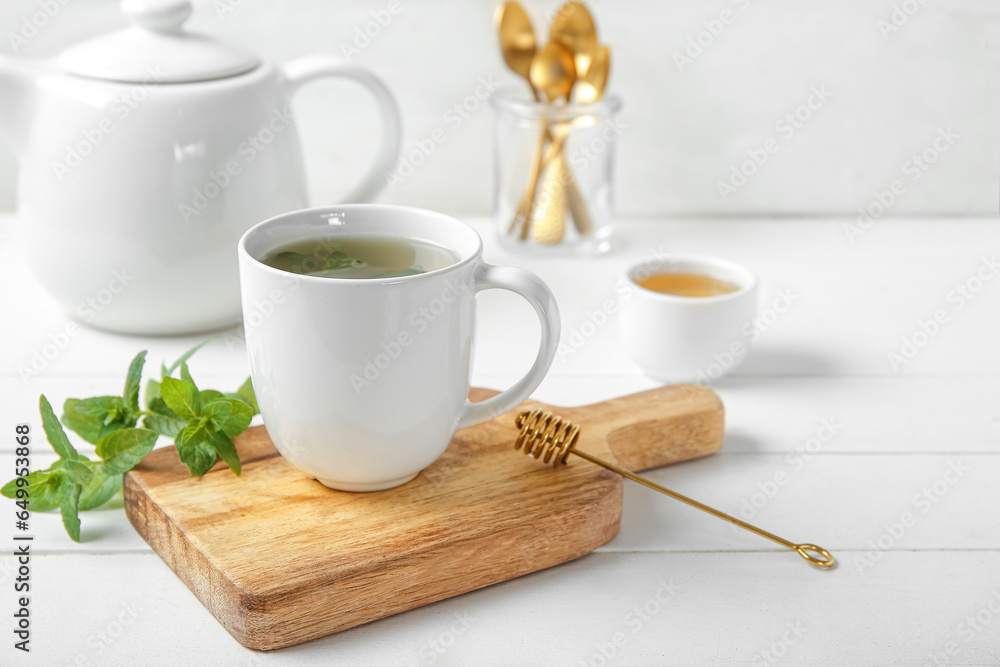 Teapot with cup of fresh mint tea, honey and spoons on white wooden table