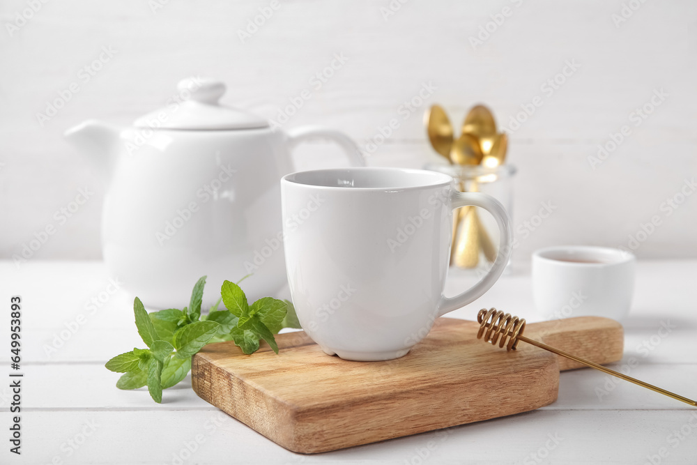 Teapot with cup of fresh mint tea, honey and spoons on white wooden table