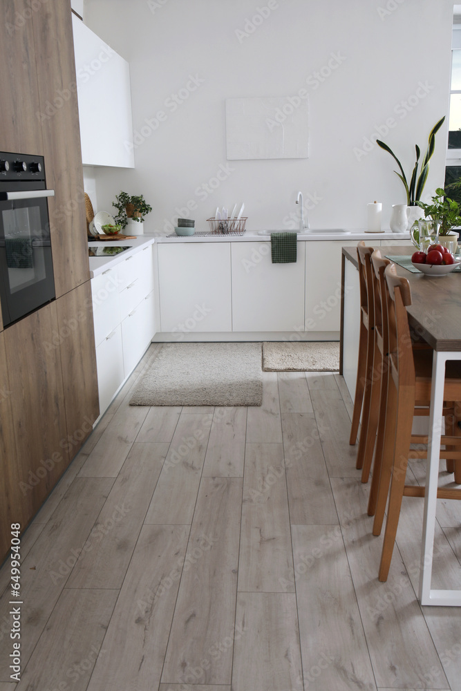 Interior of modern kitchen with white counters, integrated oven and island table