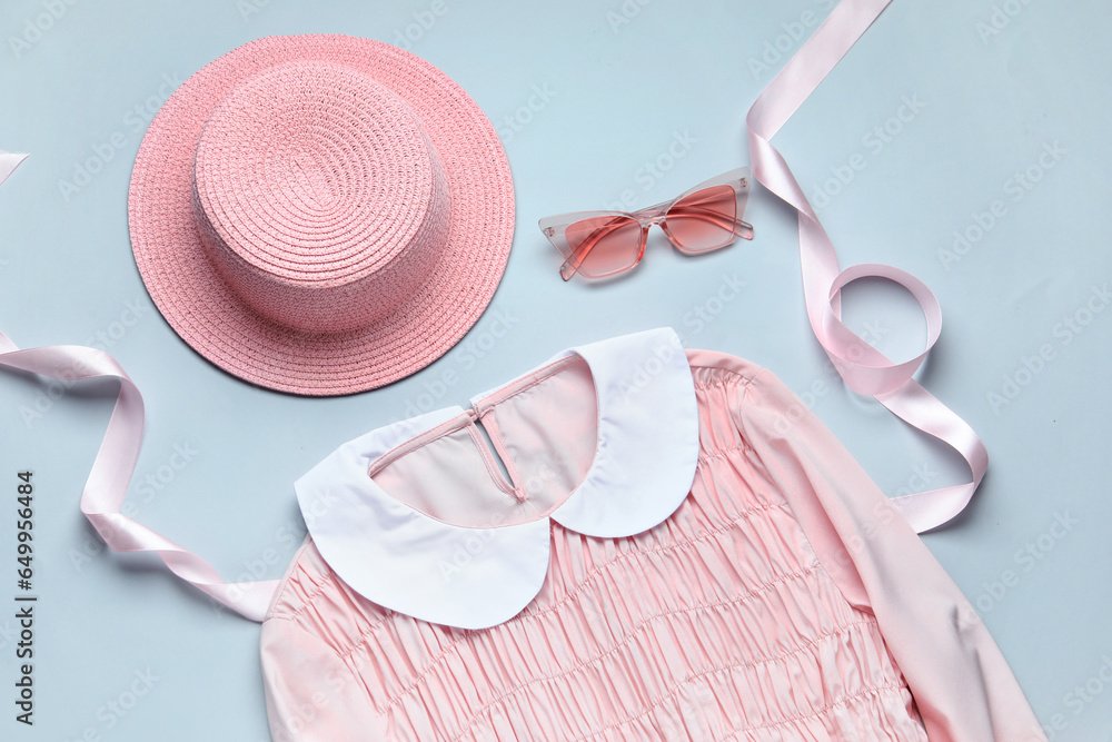 Pink wicker hat, sunglasses and dress on blue background