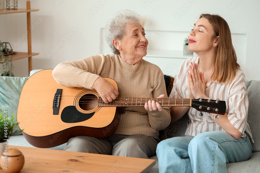 Young woman and her grandmother playing guitar at home