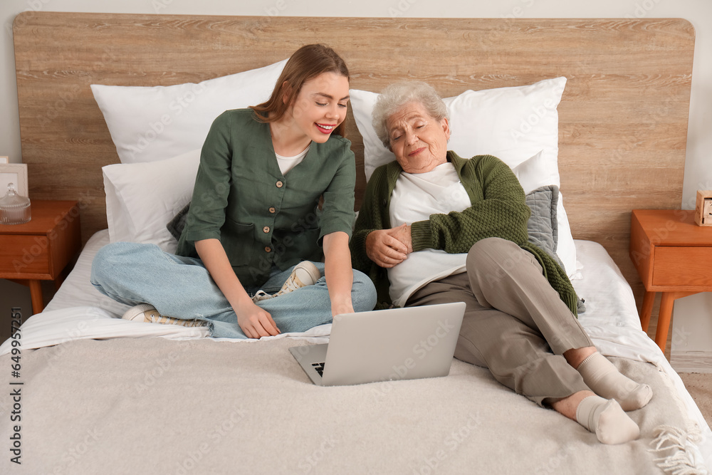 Young woman with her grandmother using laptop in bedroom