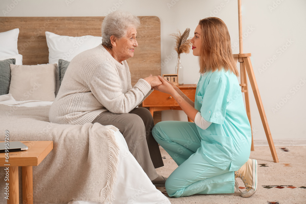 Senior woman with caregiver holding hands in bedroom