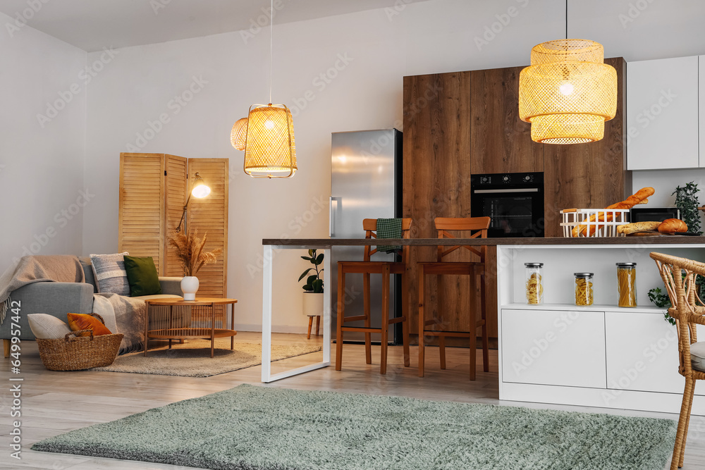 Interior of modern open space kitchen with grey sofa, island and glowing lamps