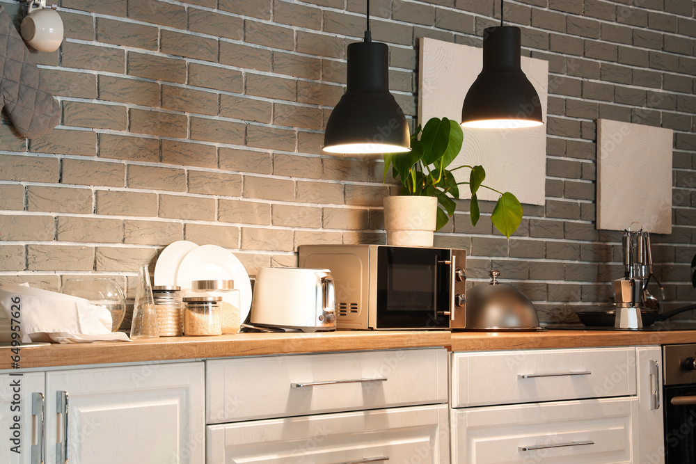 Interior of modern kitchen with glowing lamps and white counters with microwave oven at evening