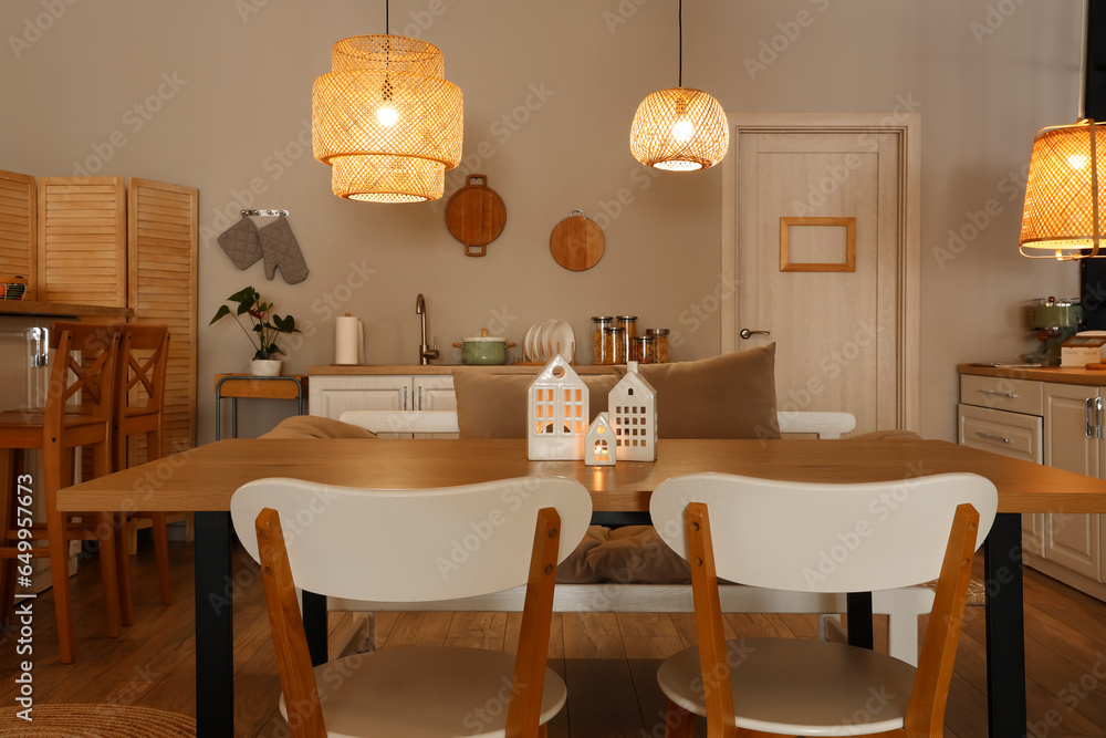 Interior of modern kitchen with glowing lamps, dining table and chairs at evening