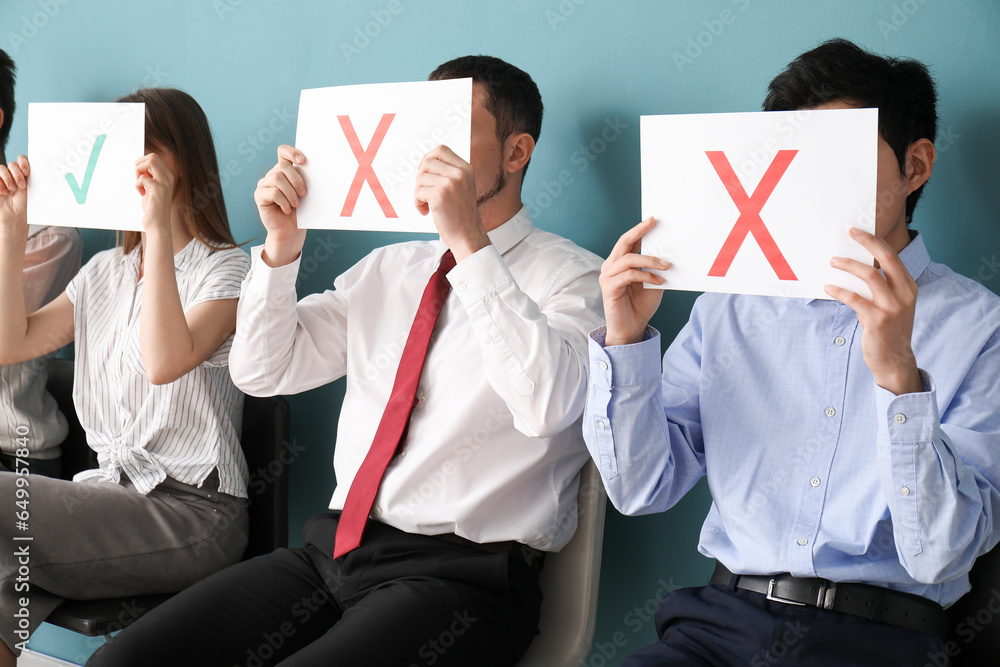 Young applicants holding paper sheets with check mark and crosses in room