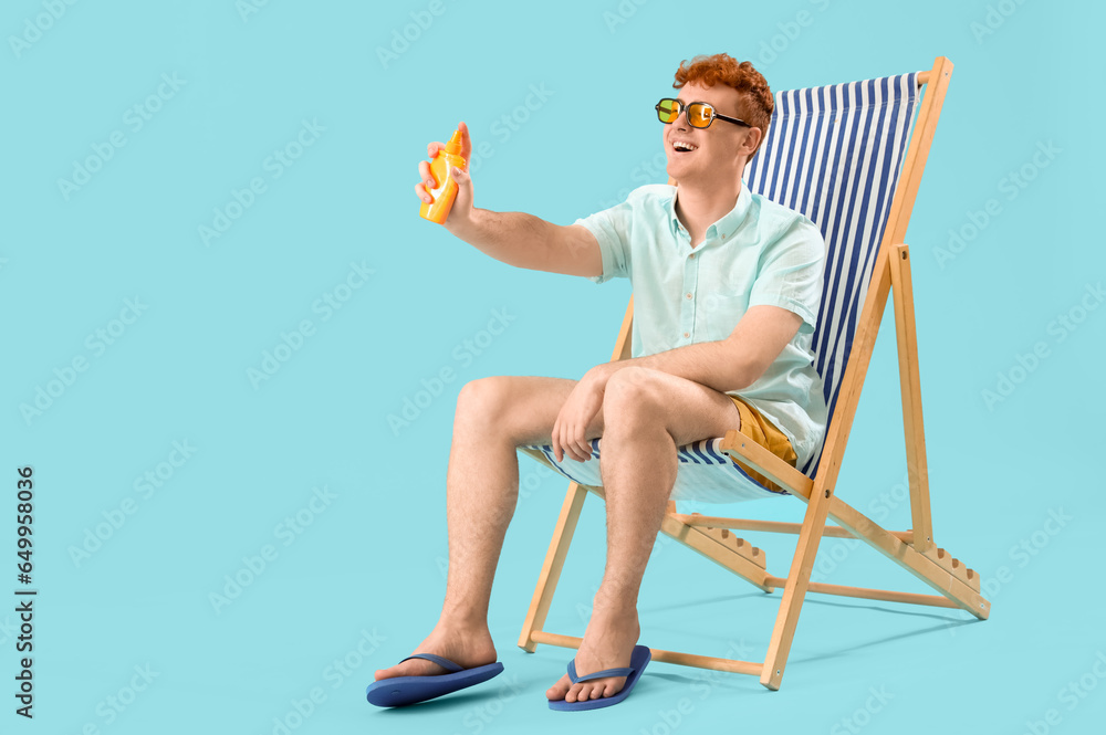 Young man with sunscreen cream in deck chair on blue background