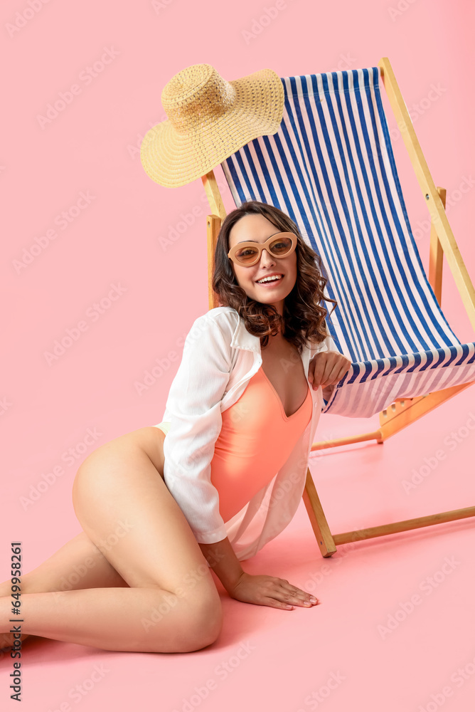 Young woman with deck chair sitting on pink background