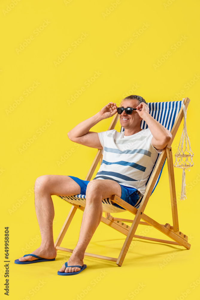 Mature man relaxing in deck chair on yellow background