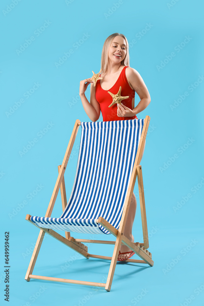 Beautiful young woman with starfishes and deck chair on blue background