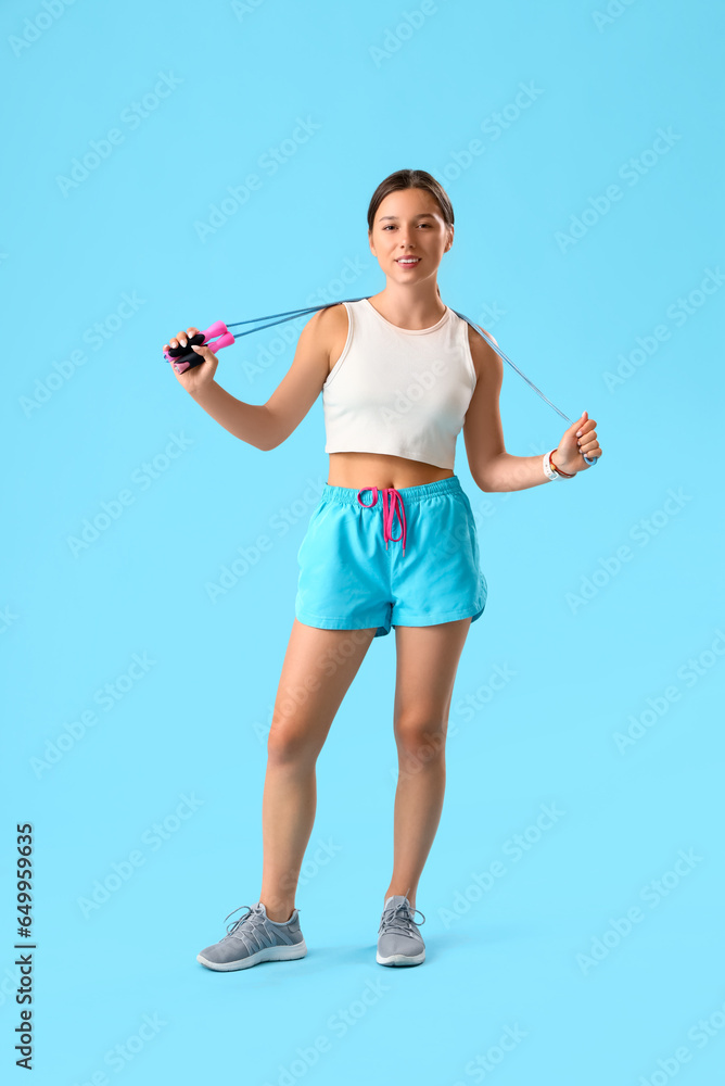 Sporty young woman with jumping rope on blue background