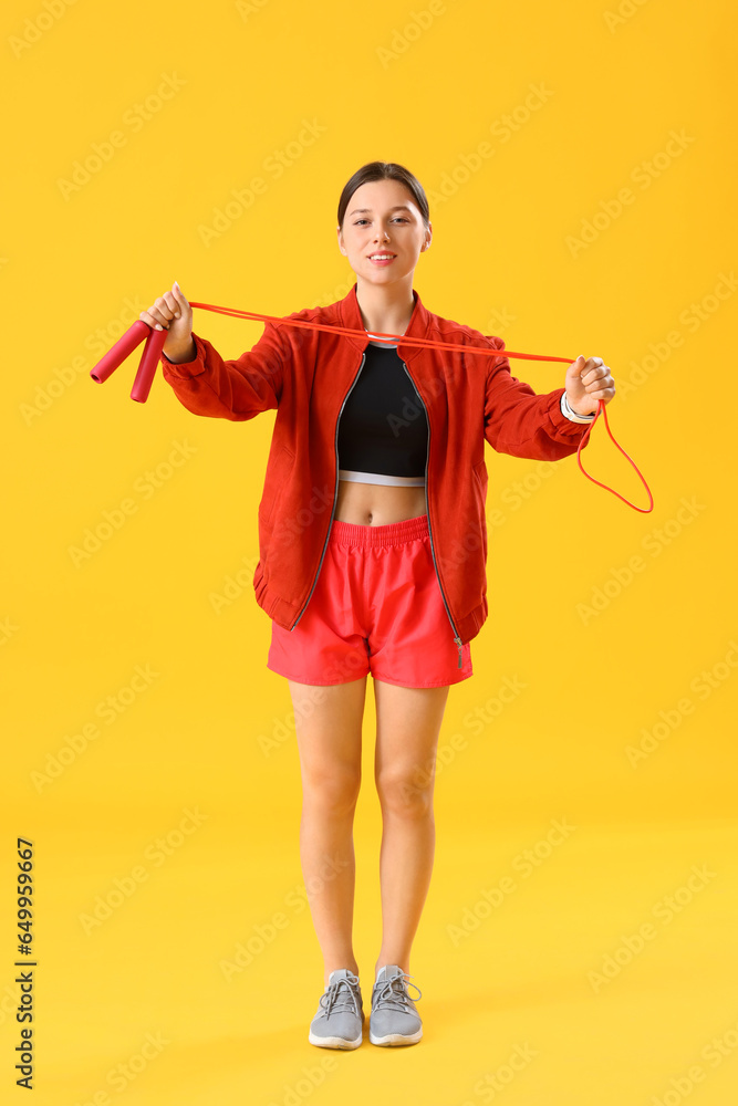 Sporty young woman with jumping rope on yellow background