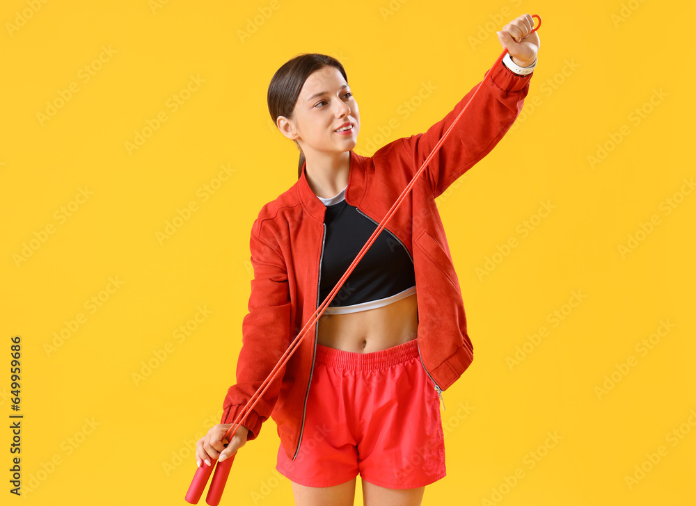 Sporty young woman with jumping rope on yellow background