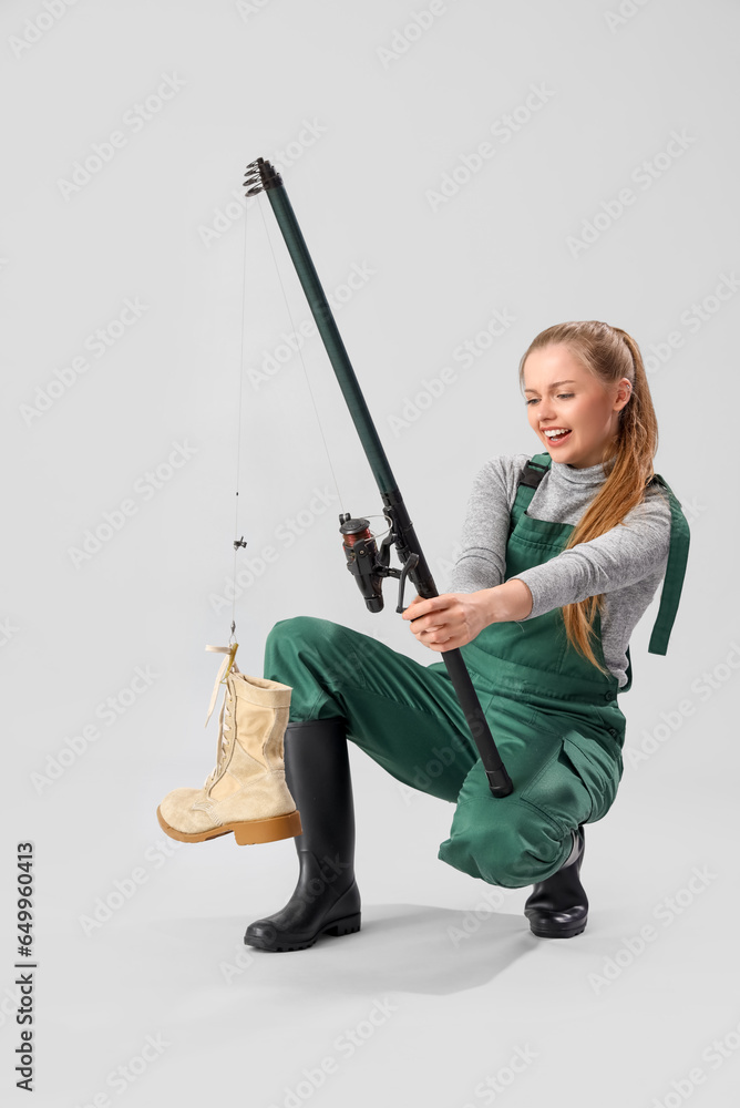 Displeased young woman catching shoe with fishing rod on light background